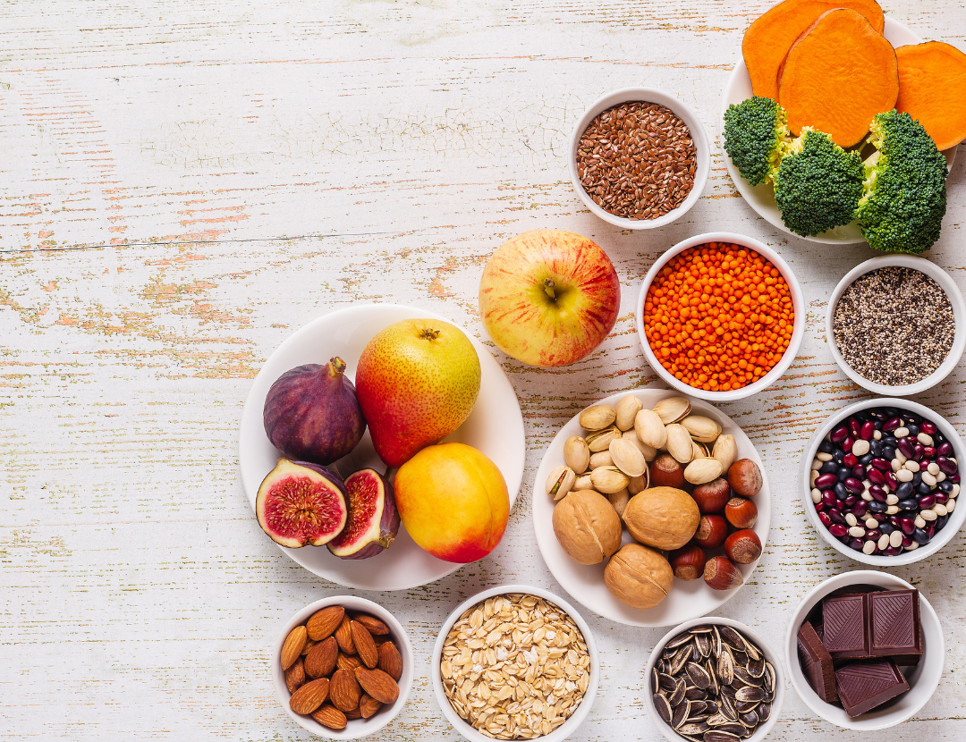 A topdown shot of various nuts, fruits and vegetables on a white wooden table.