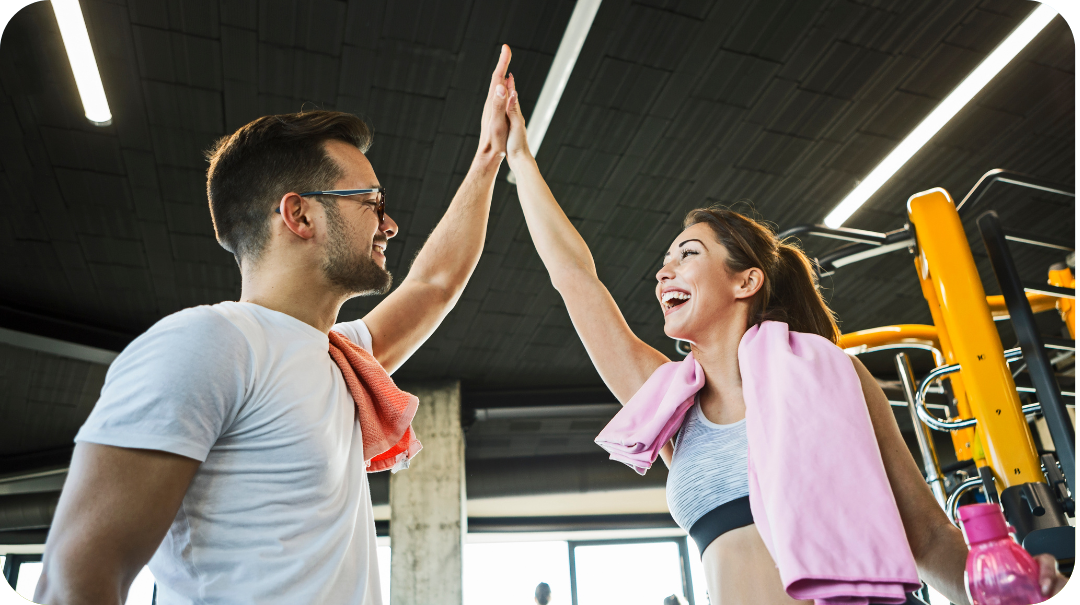 A man and a woman wearing fitness attire, smiling at each other and high fiving